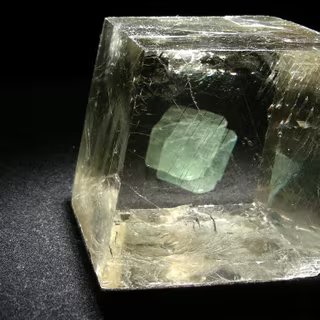 Avec l'octaèdre de fluorine verte placé derrière, on voit bien la biréfringence de la calcite optique ou spath d'Islande. © www.carionmineraux.com