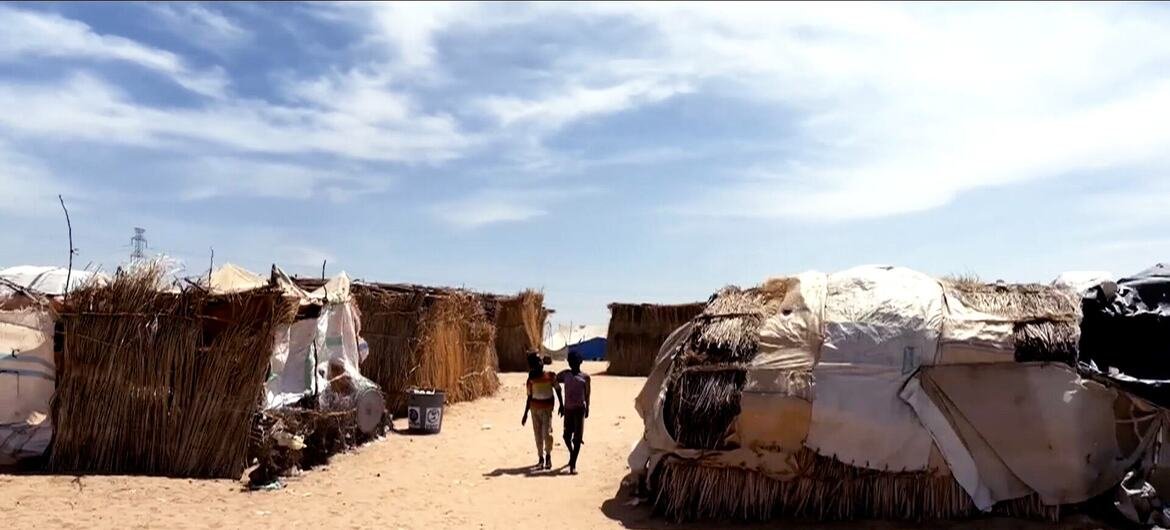 Deux enfants marchent le long d'un sentier sablonneux entre des abris temporaires dans le camp de déplacés de Goz Al Salam, dans l'État du Nil Blanc, au Soudan.