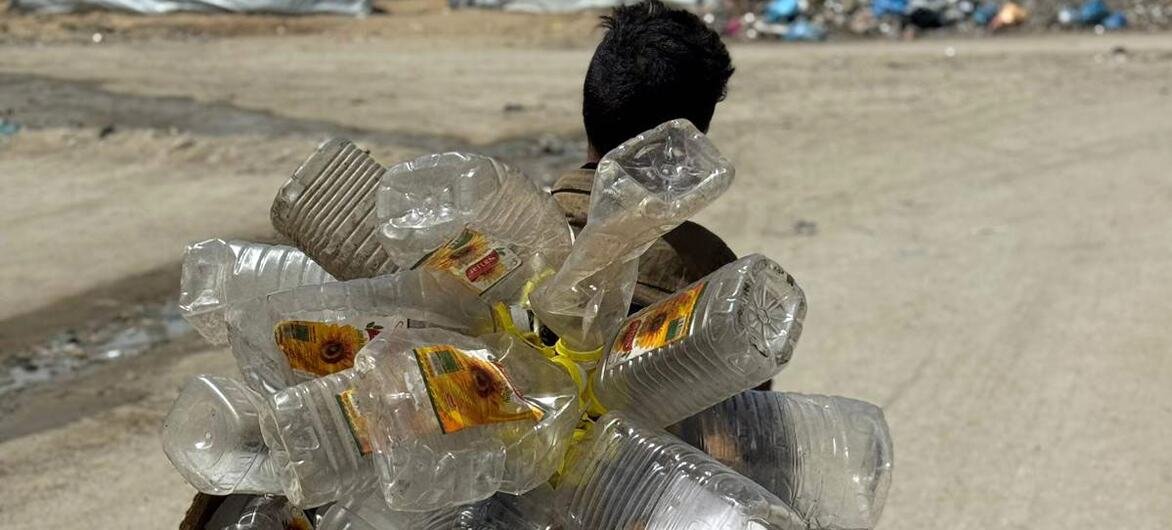 Un jeune garçon palestinien de Gaza s'éloigne de la caméra, portant sur le dos un gros paquet de bouteilles en plastique et de carton qu'il collecte comme combustible au milieu de la dévastation qui ravage sa communauté.