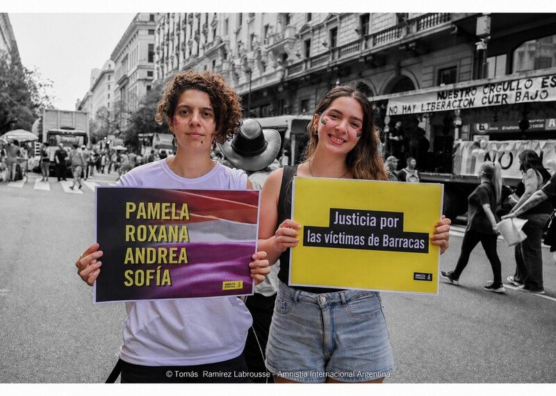 Two people hold up colourful signs calling for justice for Pamela, Roxana, Andrea and Sofia.