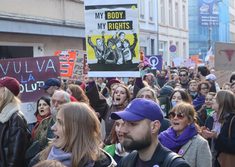 A group f people march down a street, holding signs that read 'My Body My Rights'.