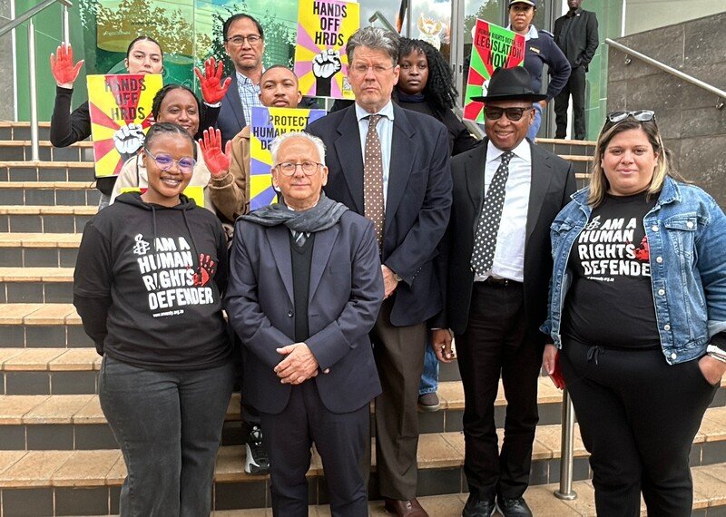 A group of people stood on steps, hold an array of banners, reading Hands of HRDS.